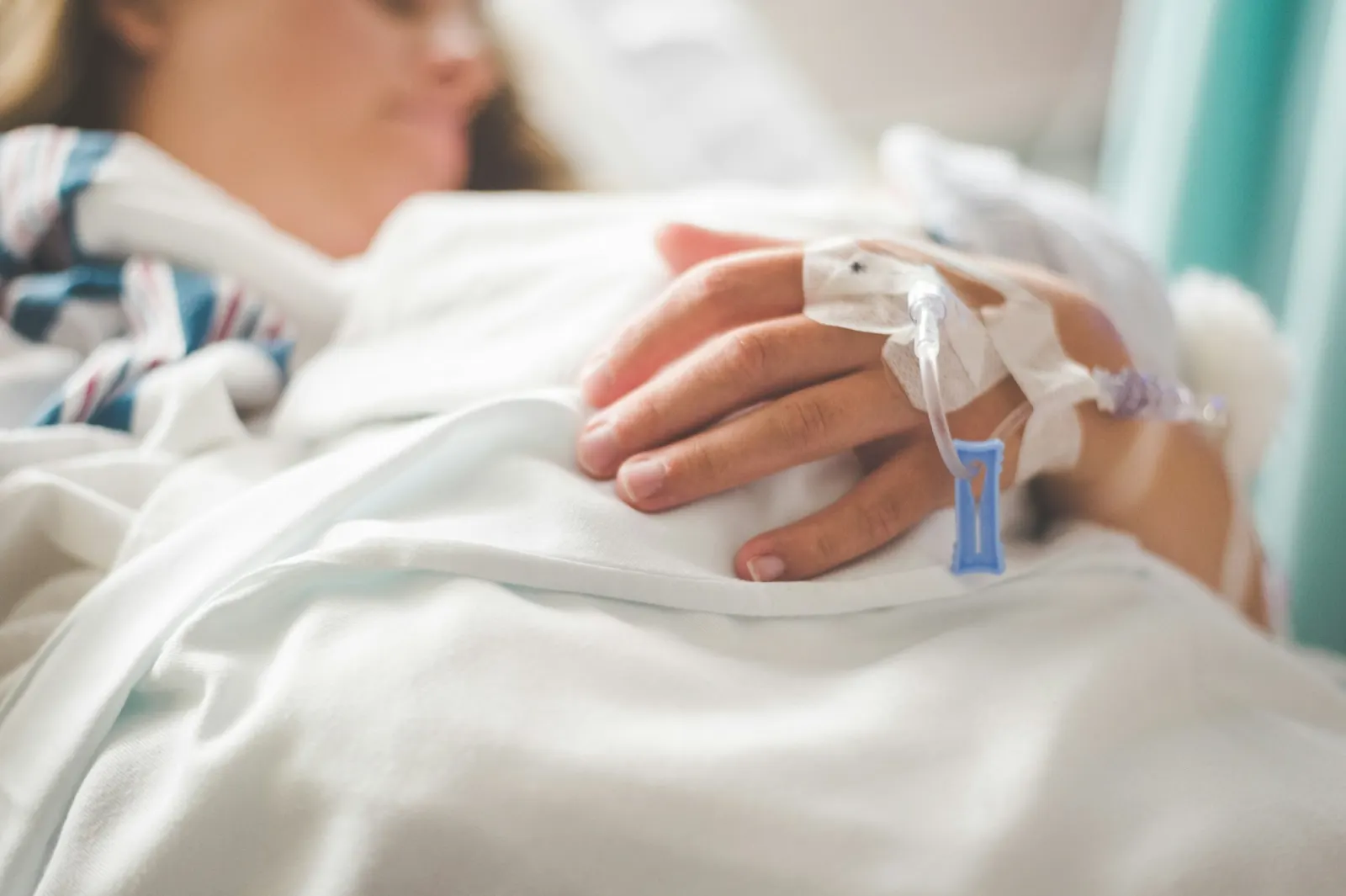 A hand with an IV line resting on white bedding
